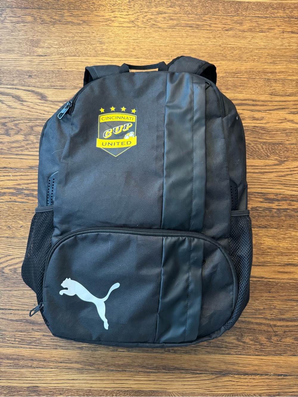 Cincinnati Cup United" soccer team crest. 
Puma Black Backpack with Yellow crest